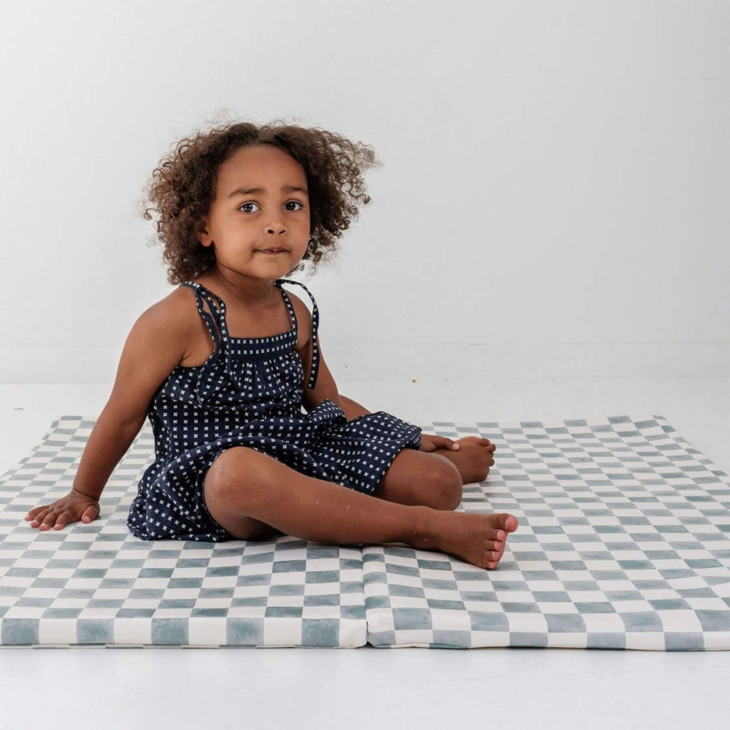 Child sitting on a checkered mat with a plain background