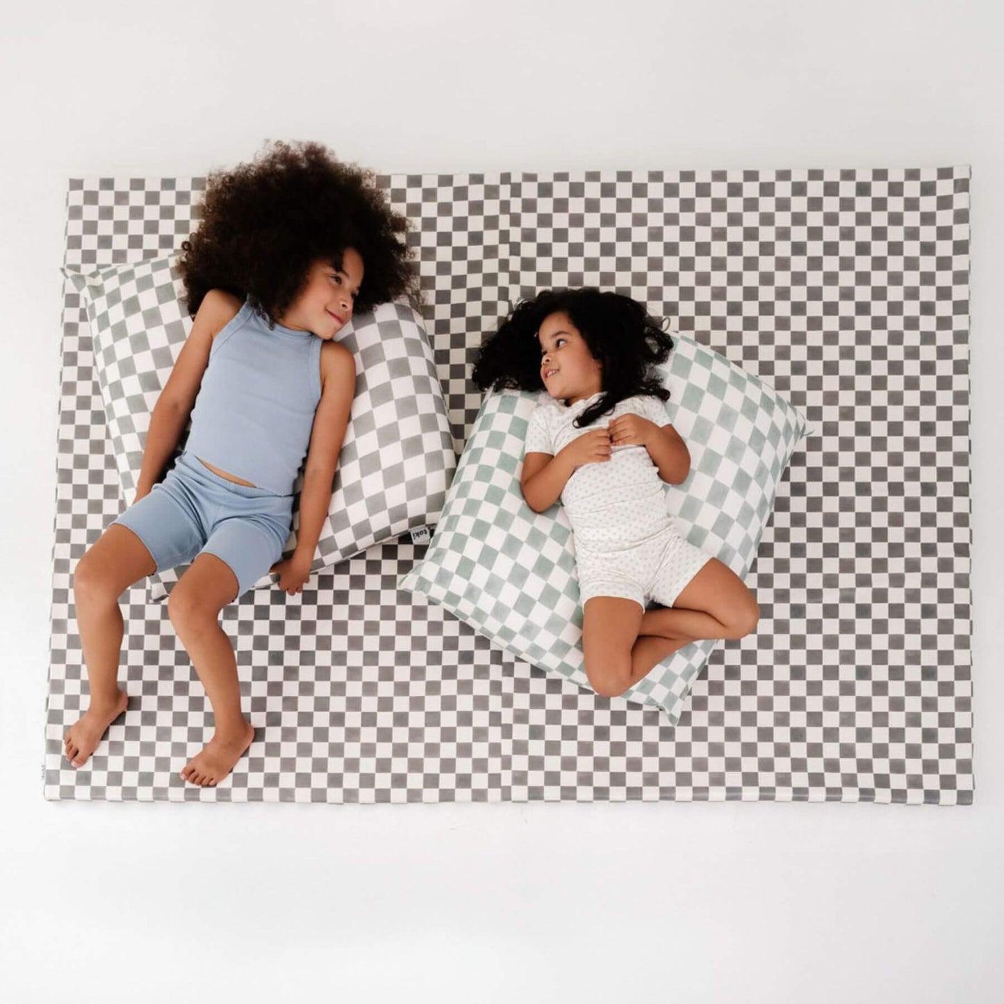 Two children sitting on a checkered mat with bean bags.
