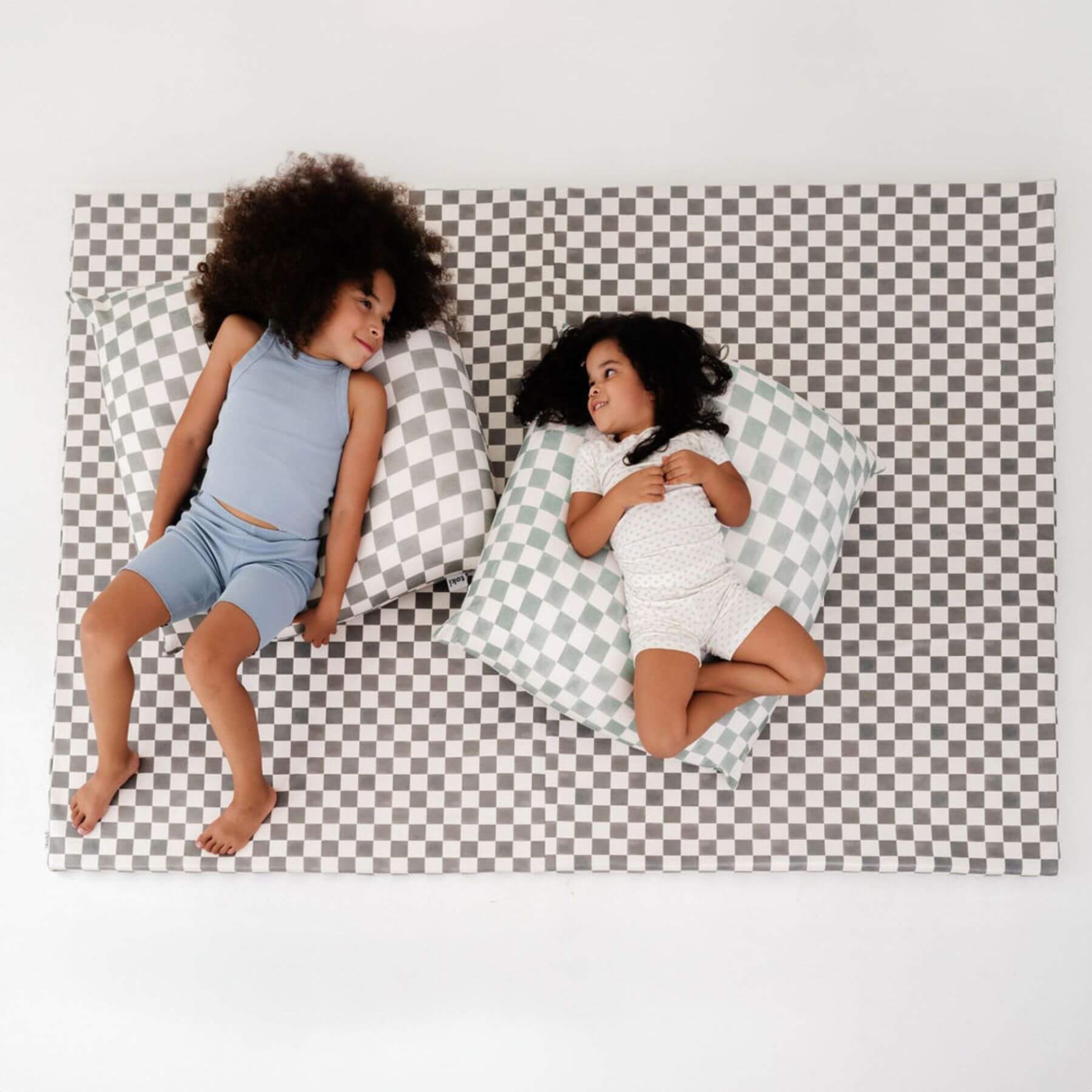 Two children sitting on a checkered mat with bean bags.