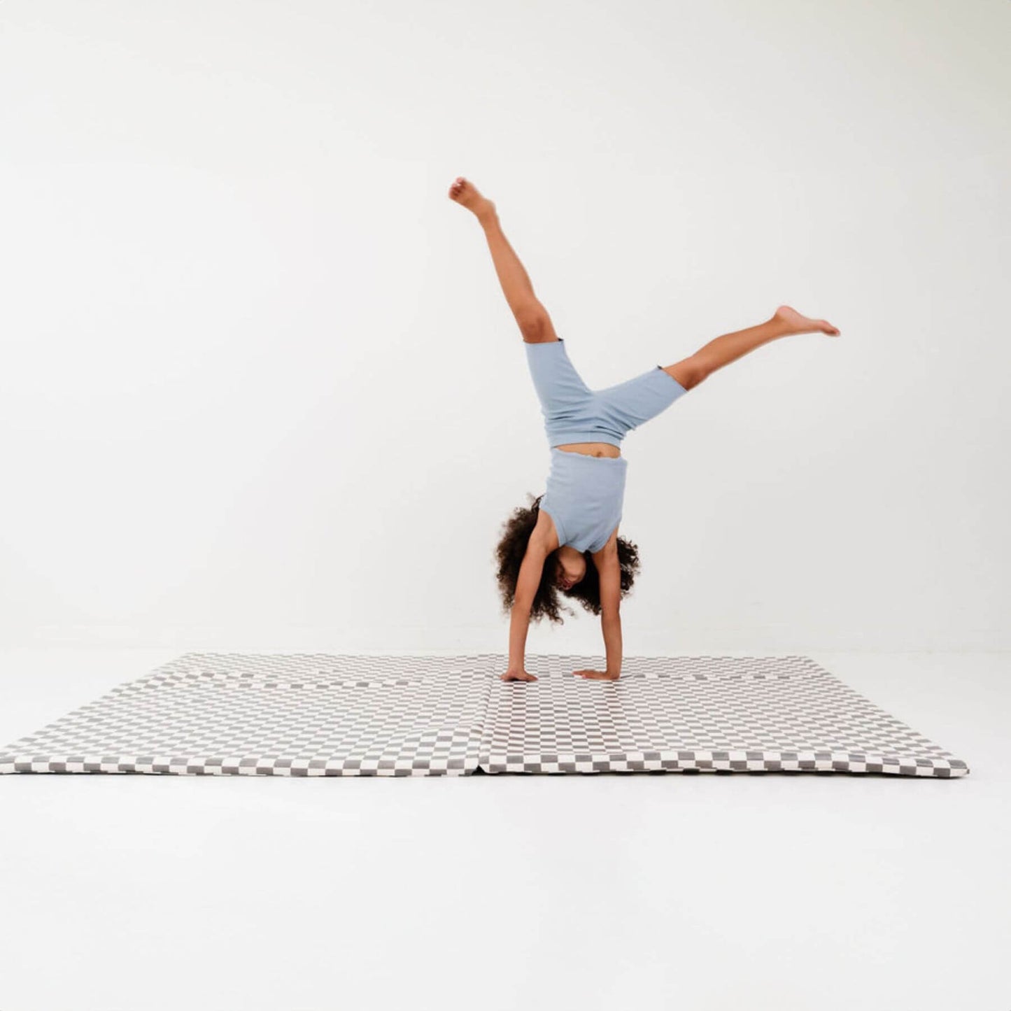Person doing a handstand on a checkered mat with a white background