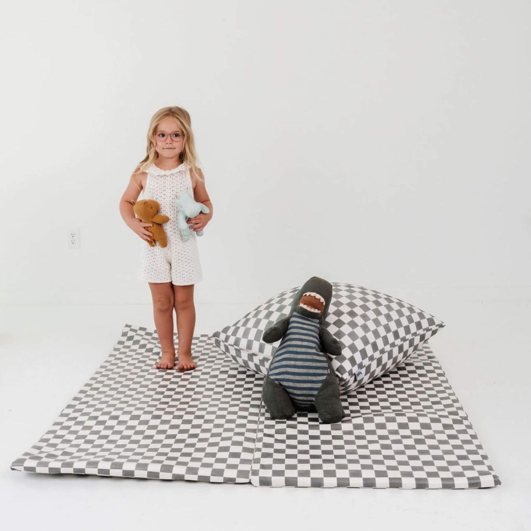 Child standing on a checkered mat with toys and pillows on a plain background