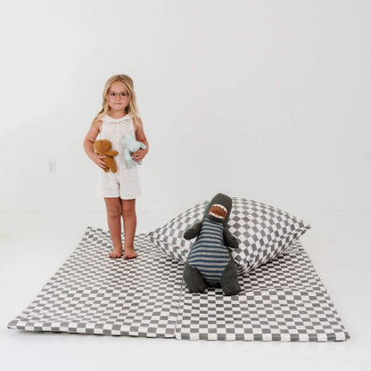 Child standing on a checkered mat with toys and pillows on a plain background