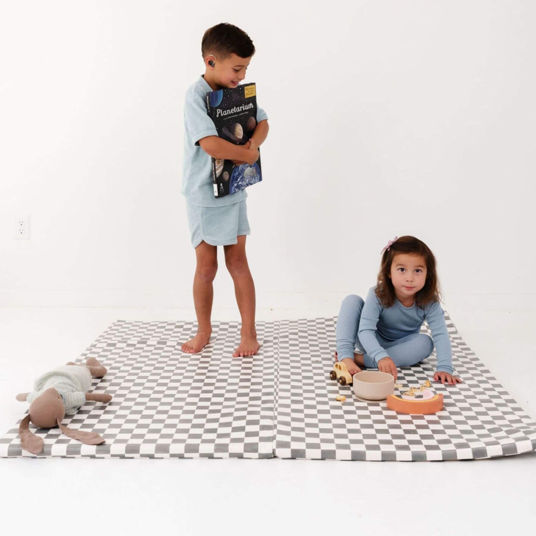 Two children on a checkered mat with toys and books