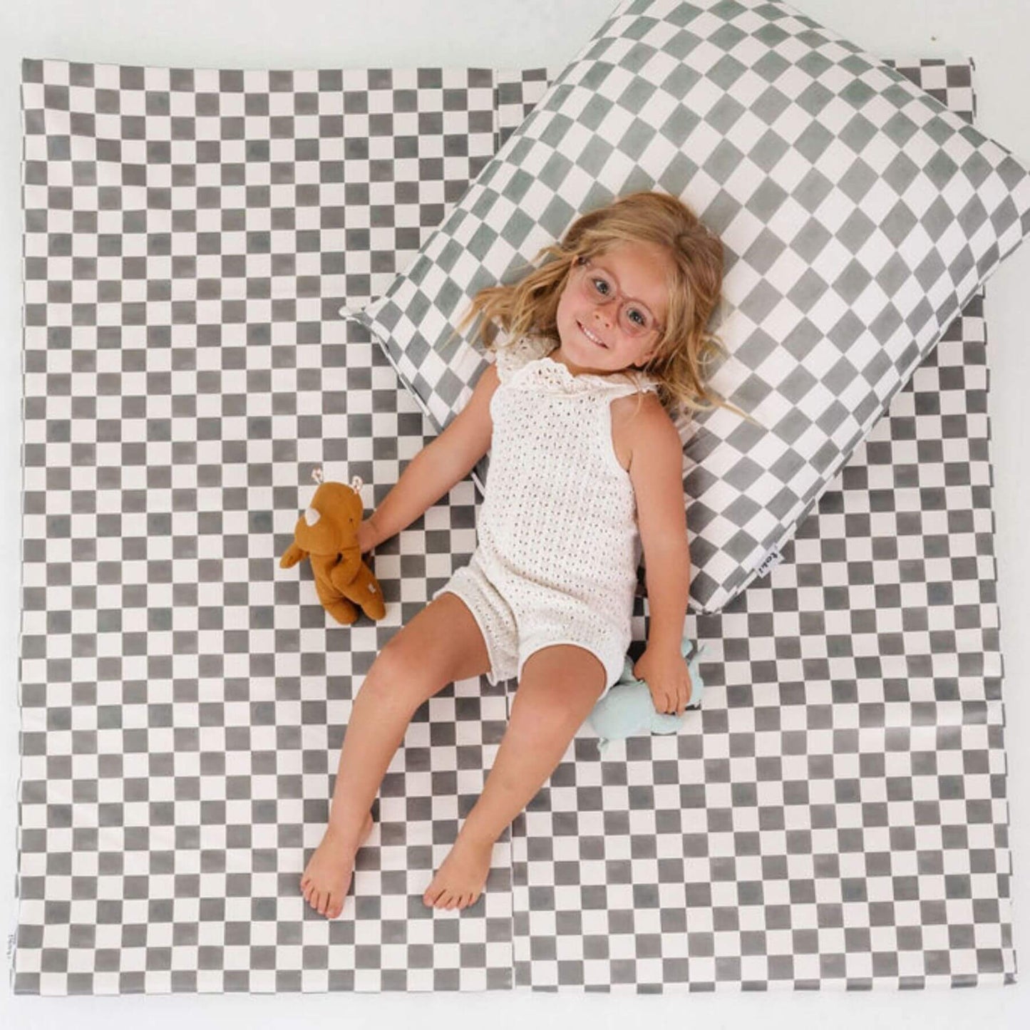 Child in a white romper lying on a checkered mat with a pillow