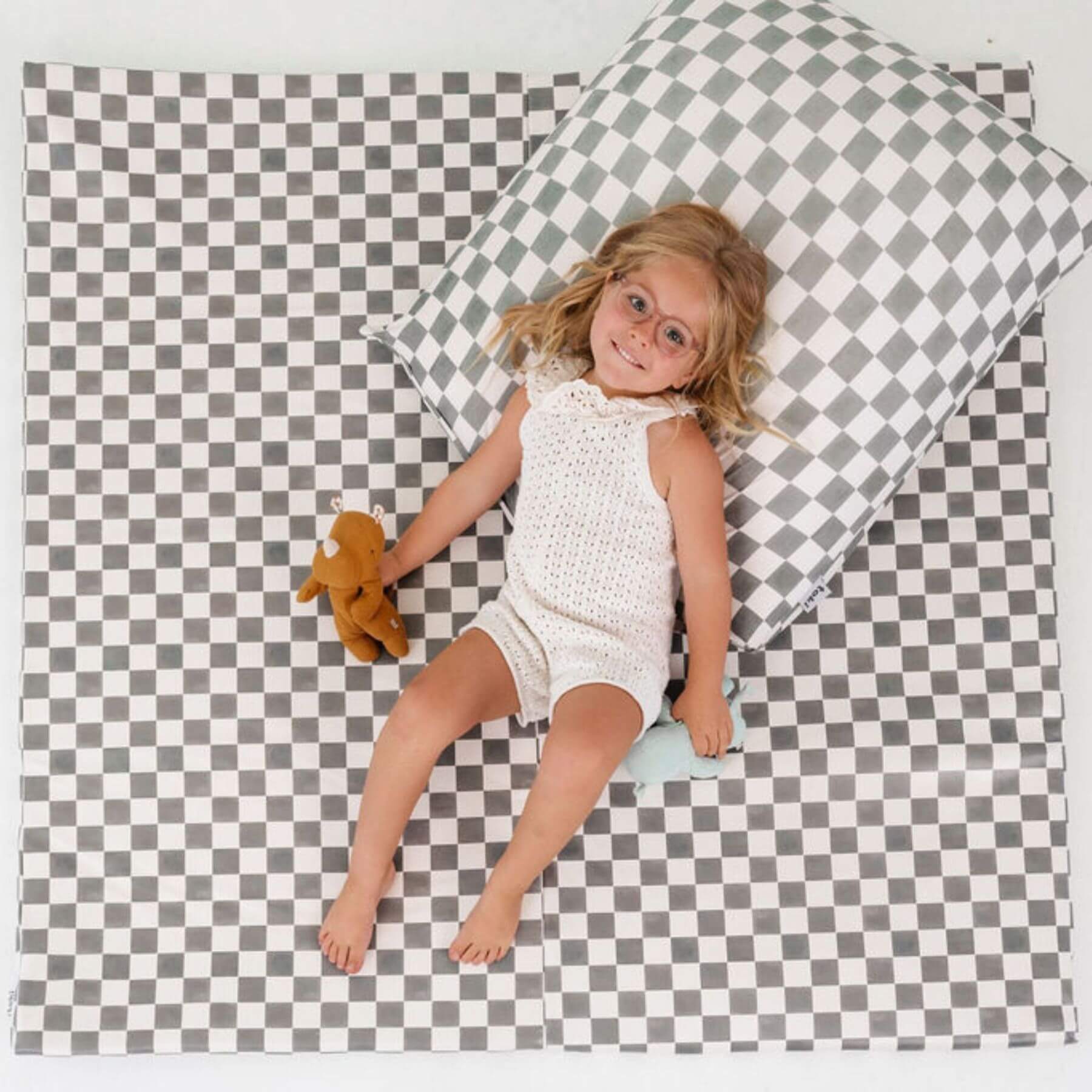 Child in a white romper lying on a checkered mat with a pillow