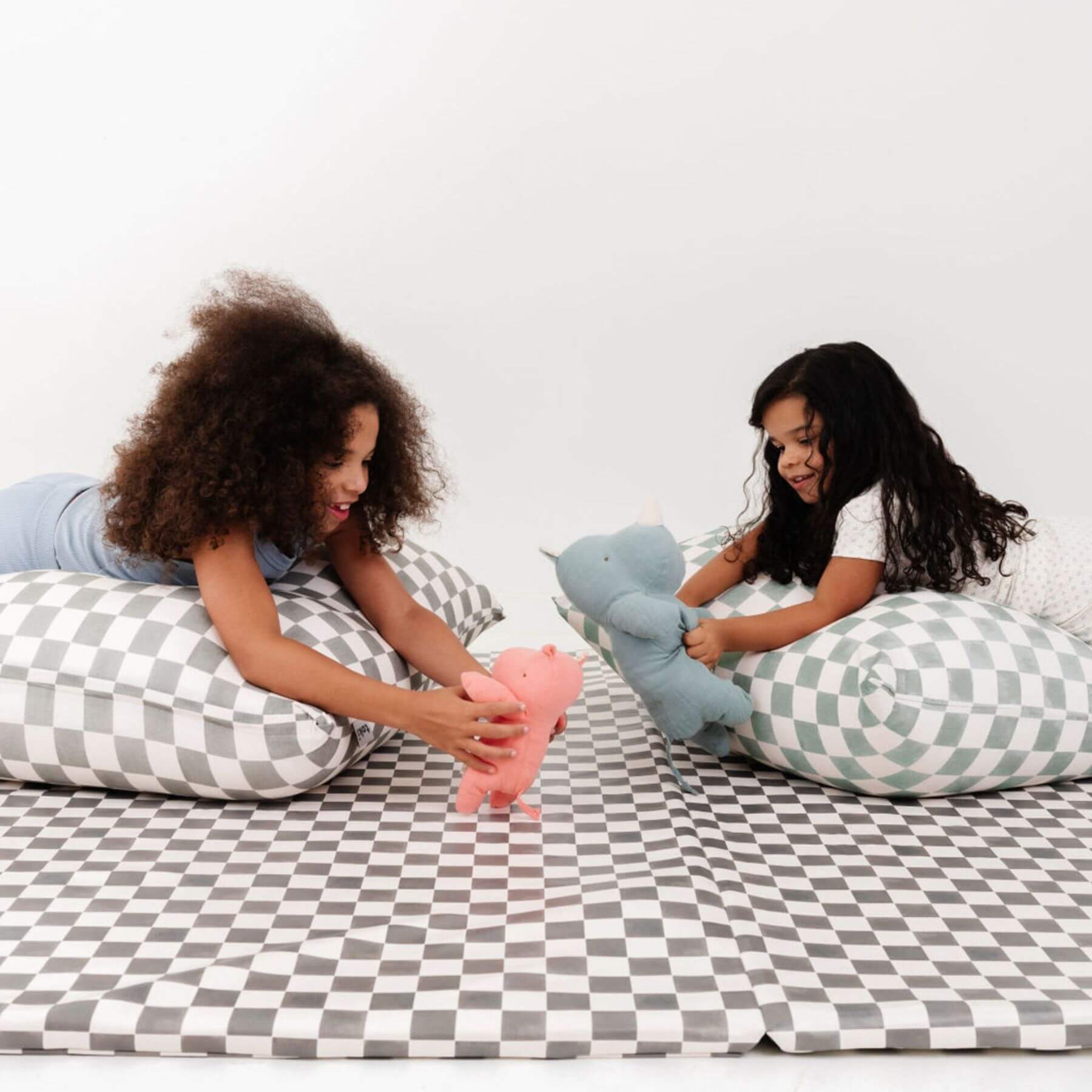 Two children playing with stuffed animals on checkered bedsheets.