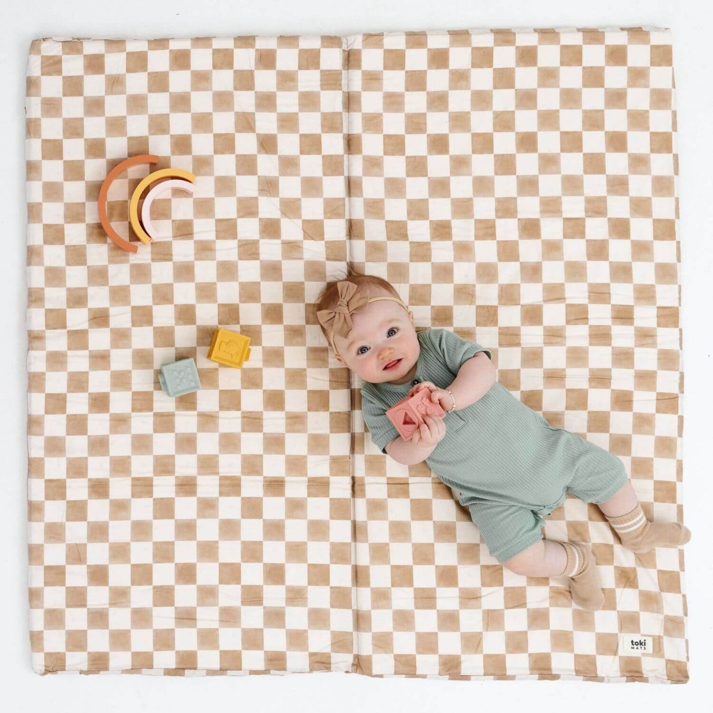 Baby lying on a checkered mat with colorful toys