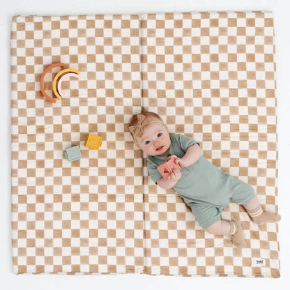 Baby lying on a checkered mat with colorful toys