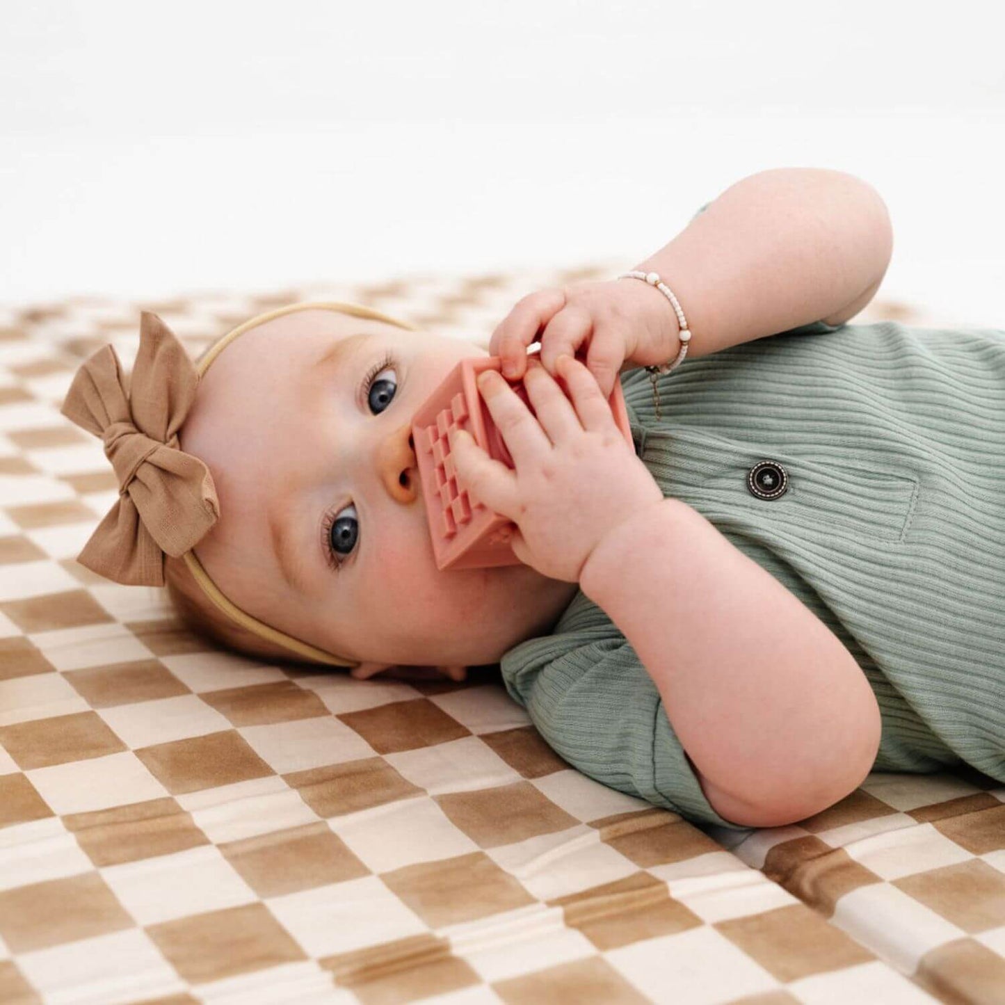Baby lying on a checkered playmat with a pink teething toy