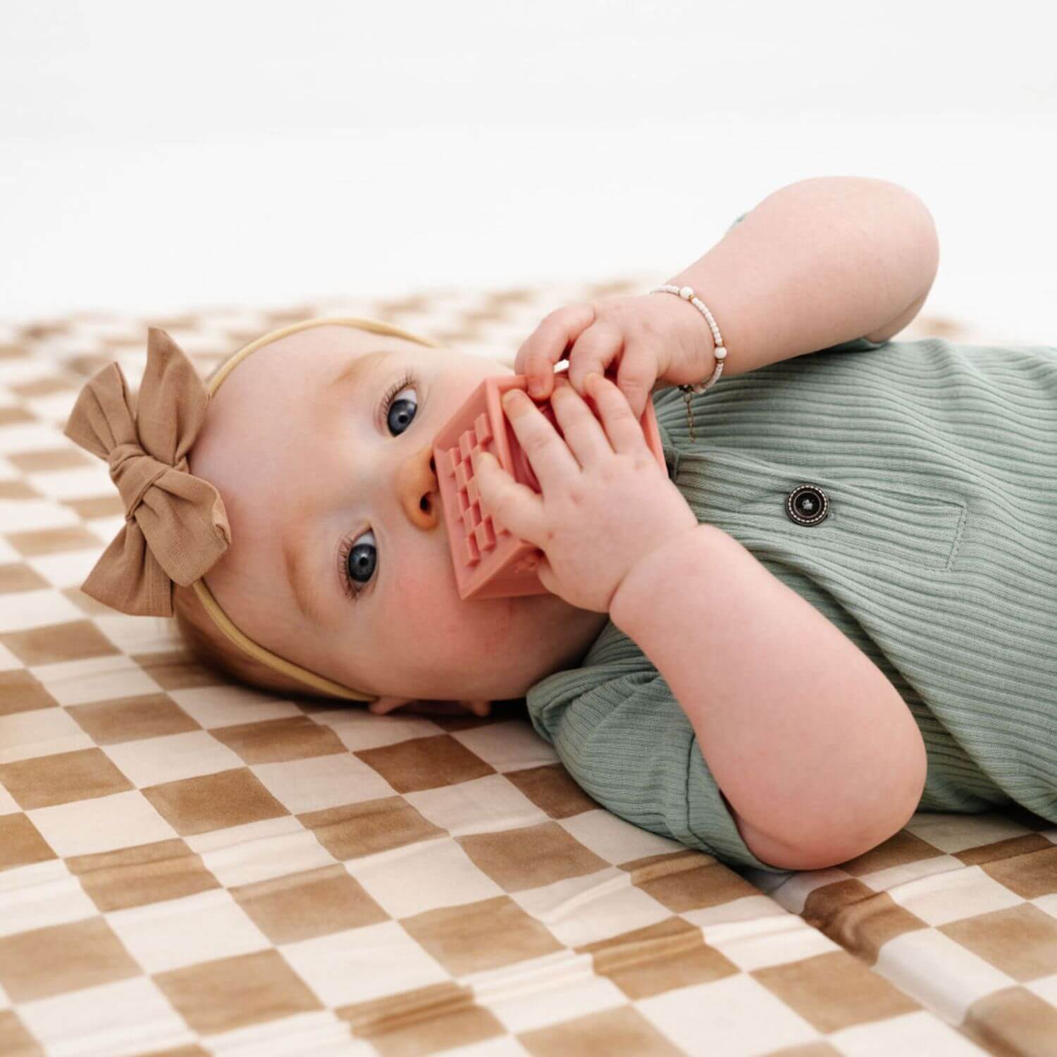 Baby lying on a checkered playmat with a pink teething toy