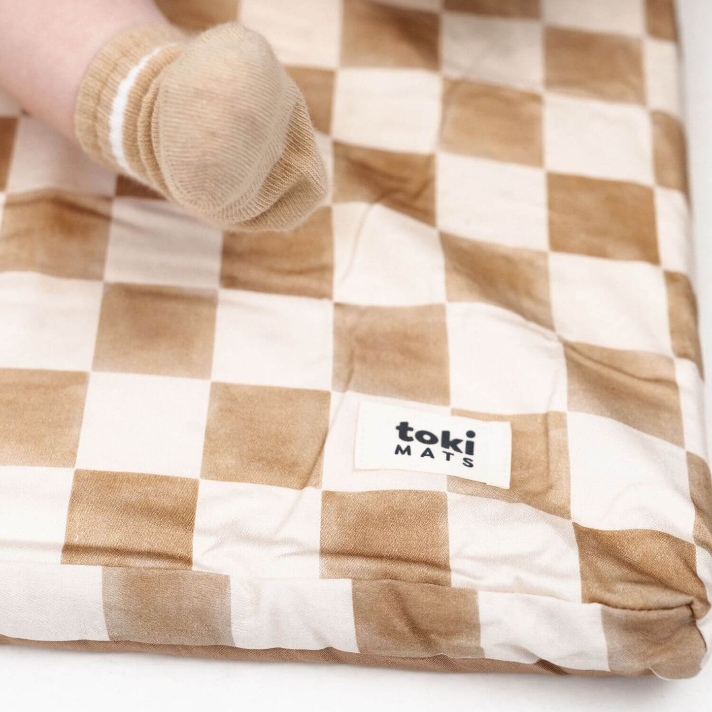 Brown and white checkered mat with 'toki MATS' logo, rolled up on a white surface.