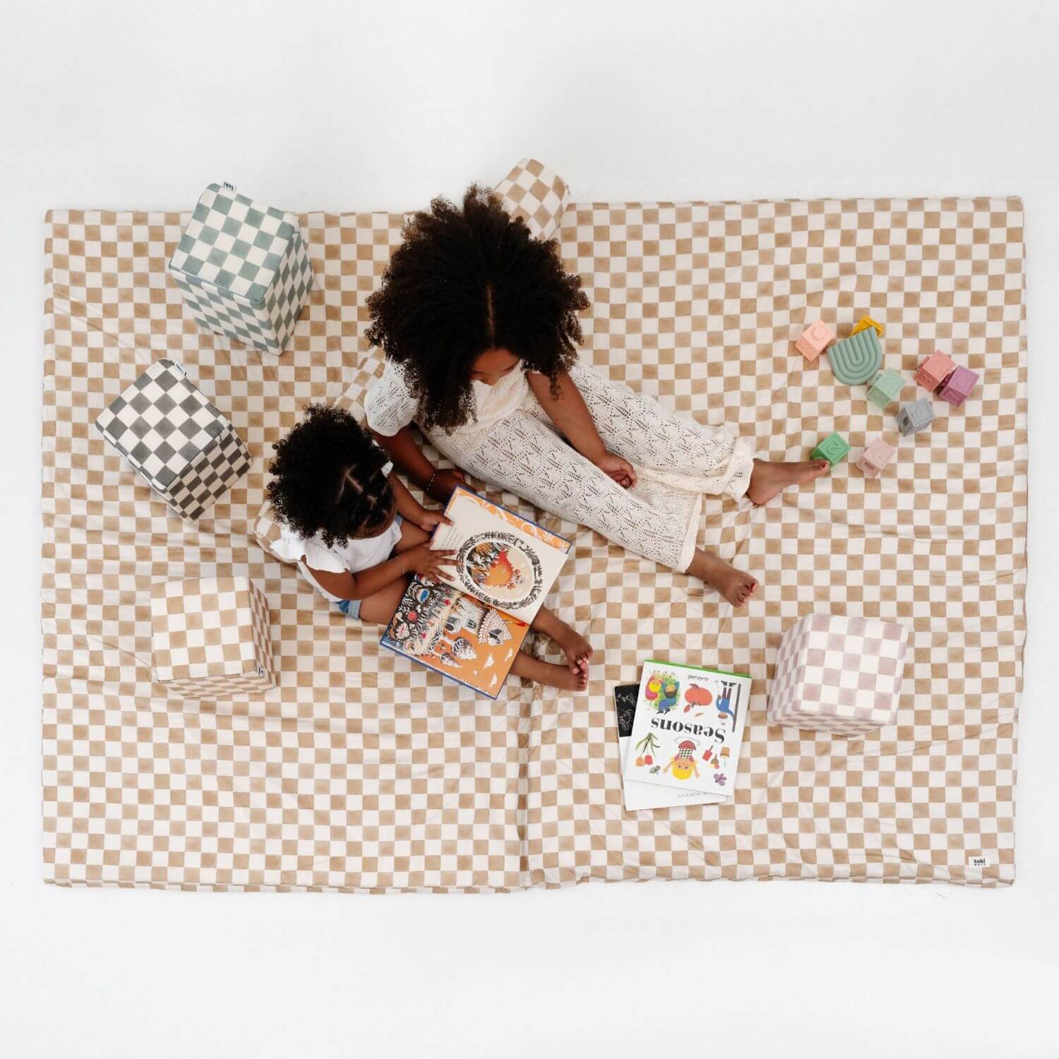 Two children sitting on Toki Kids Checker Toffee Organic Cotton Mat with books and toys around them.