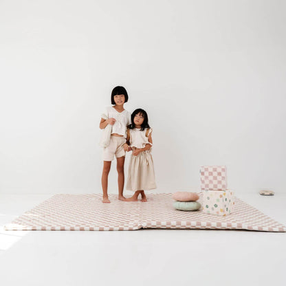 Two children standing on Toki Kids Checker Toffee Vegan Leather Mat with colorful pillows against a white background