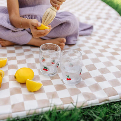 Person squeezing a lemon over two glasses on Toki Kids Checker Toffee Vegan Leather Mat outdoors