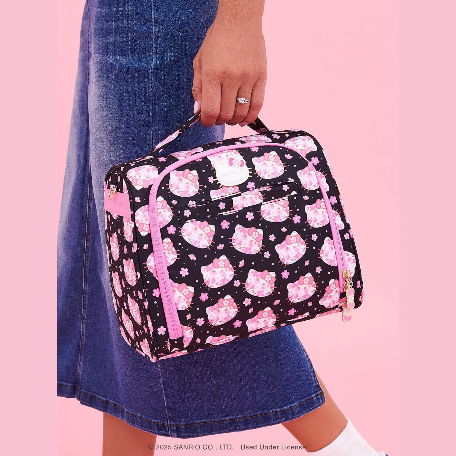 A person holds Hello Kitty® × JuJuBe Cherry Blossoms Insulated Bottle Bag, set against a solid pink background.