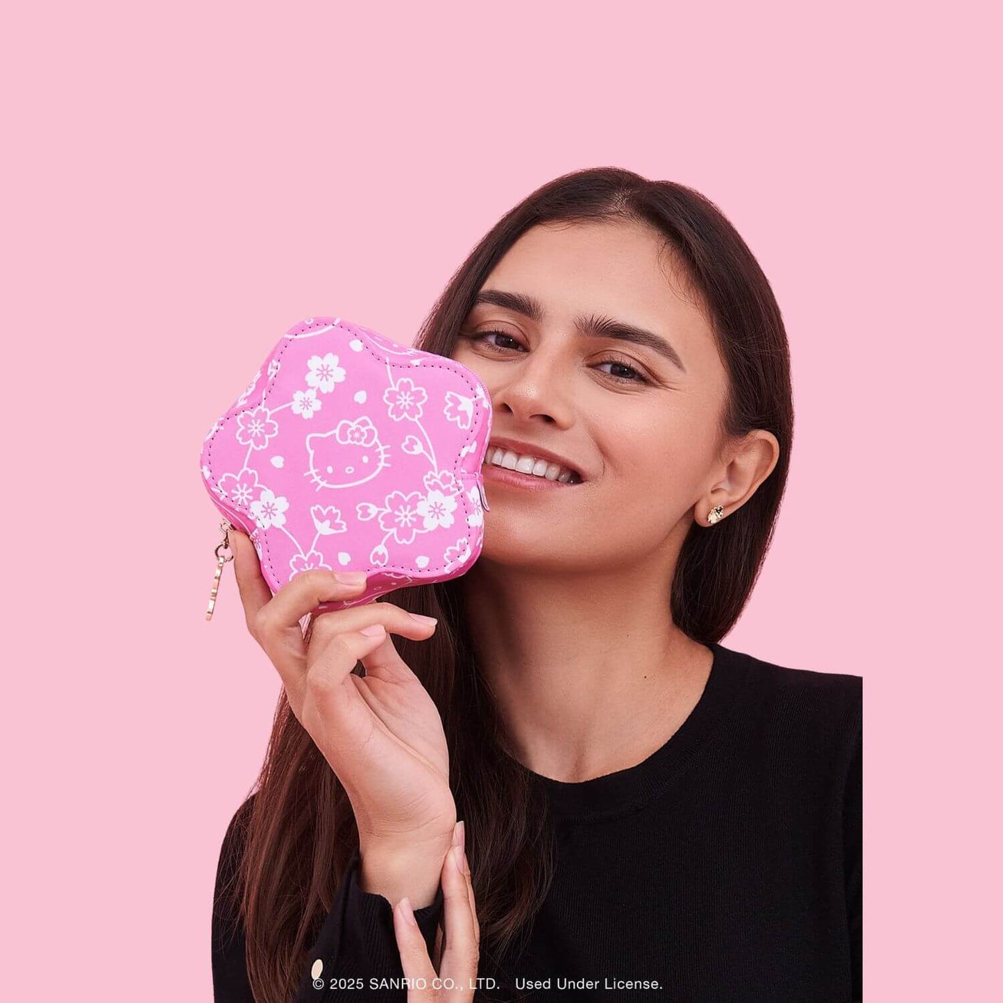 A woman holding Hello Kitty® × JuJuBe Cherry Blossoms Flower Mini Bag against a solid pink background.