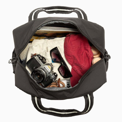 Black backpack with items like a camera, sunglasses, and a red cap inside