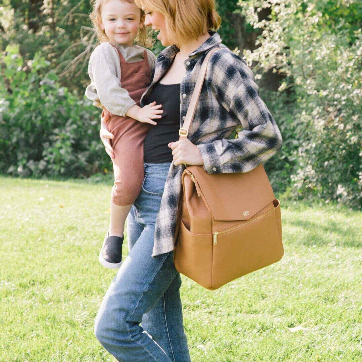 Woman holding a child and Butterscotch Classic Diaper Bag II in a park