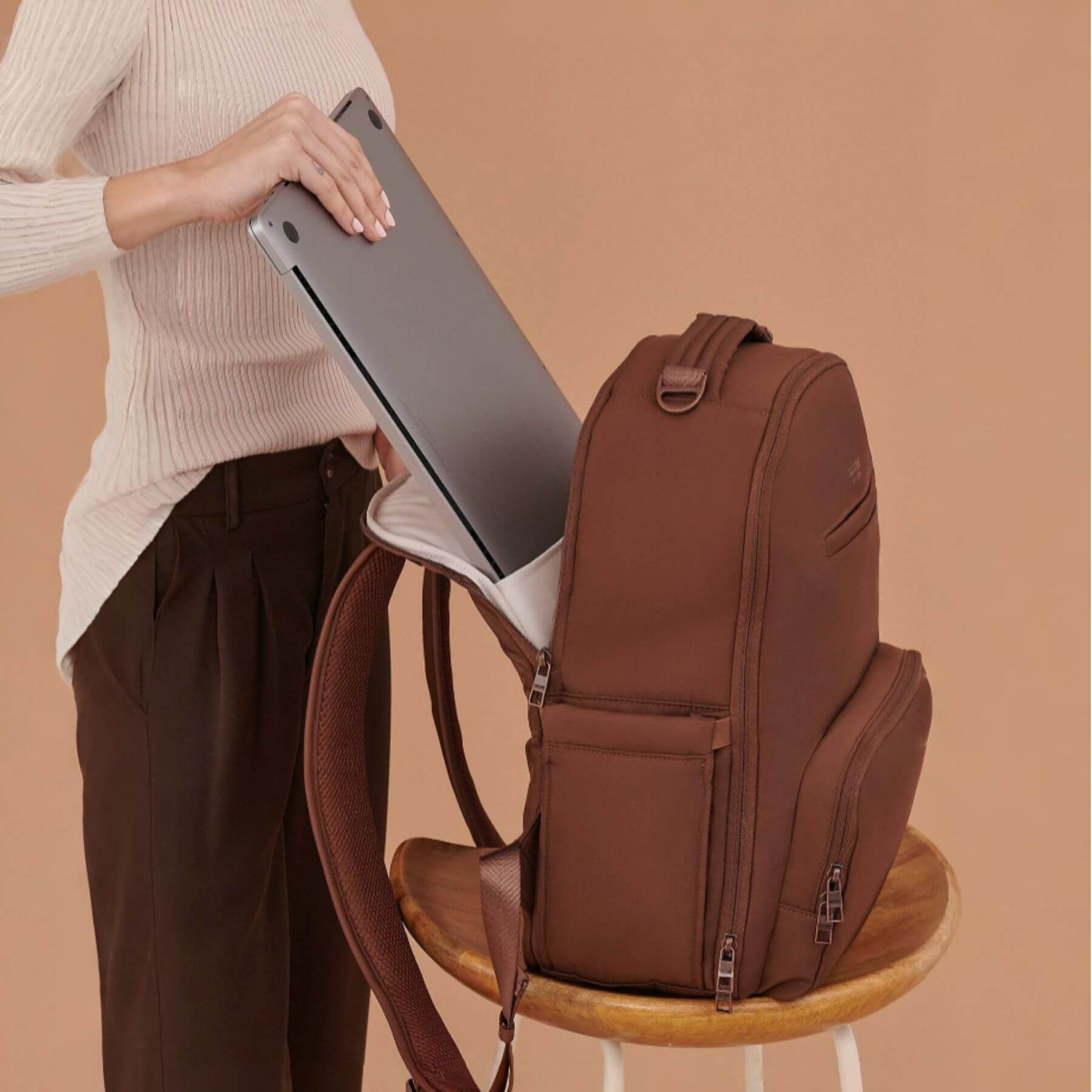 JuJuBe Classic Diaper Backpack Espresso on a stool with a person holding a laptop.