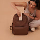 Woman sitting on the floor with JuJuBe Classic Diaper Backpack Espresso against a beige background