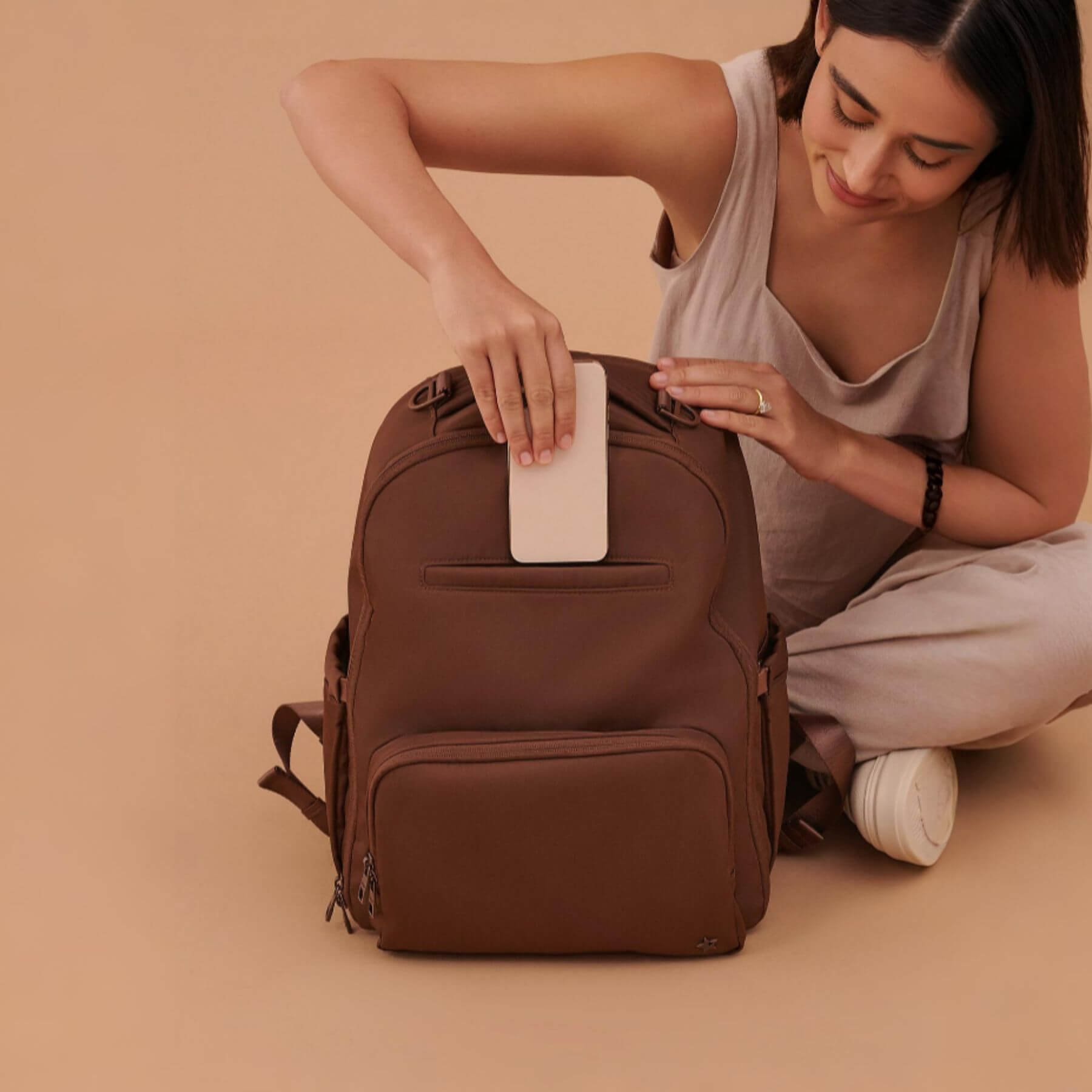 Woman sitting on the floor with JuJuBe Classic Diaper Backpack Espresso against a beige background