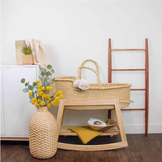 Plum+Sparrow Classic Rocking Moses Bassinet Stand with brake Natural, vase, and decorative items against a white wall.