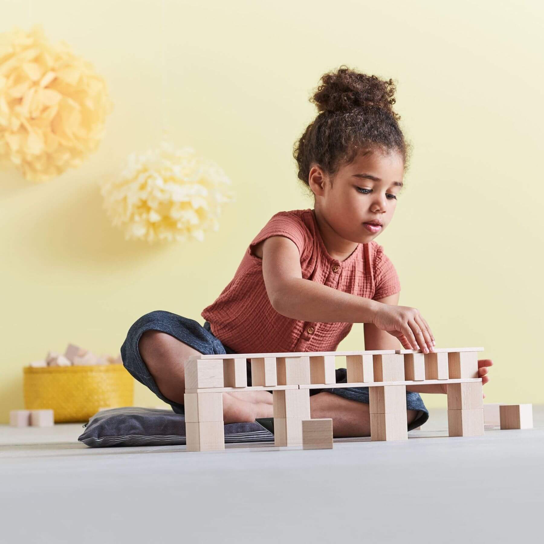 Child playing with HABA USA Clever Up! Building Block System 3.0 on a light-colored floor with a yellow wall in the background