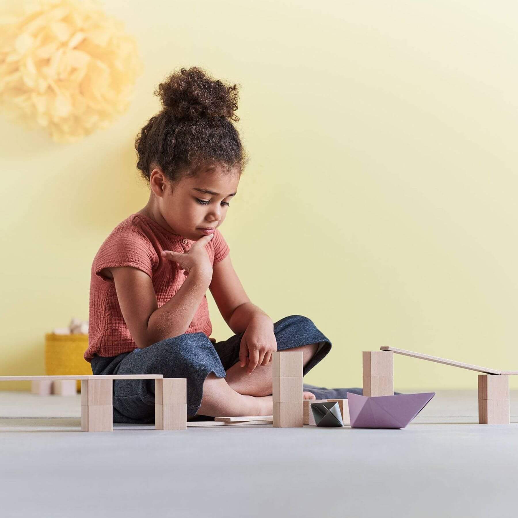 Child playing with HABA USA Clever Up! Building Block System 3.0 on a light surface with a yellow wall in the background