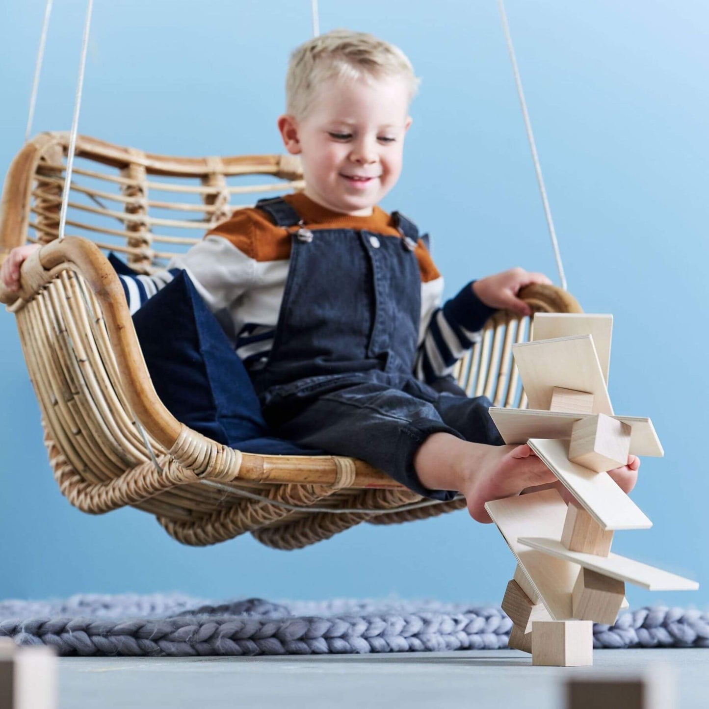 Child playing with wooden blocks in a wicker chair against a blue wall