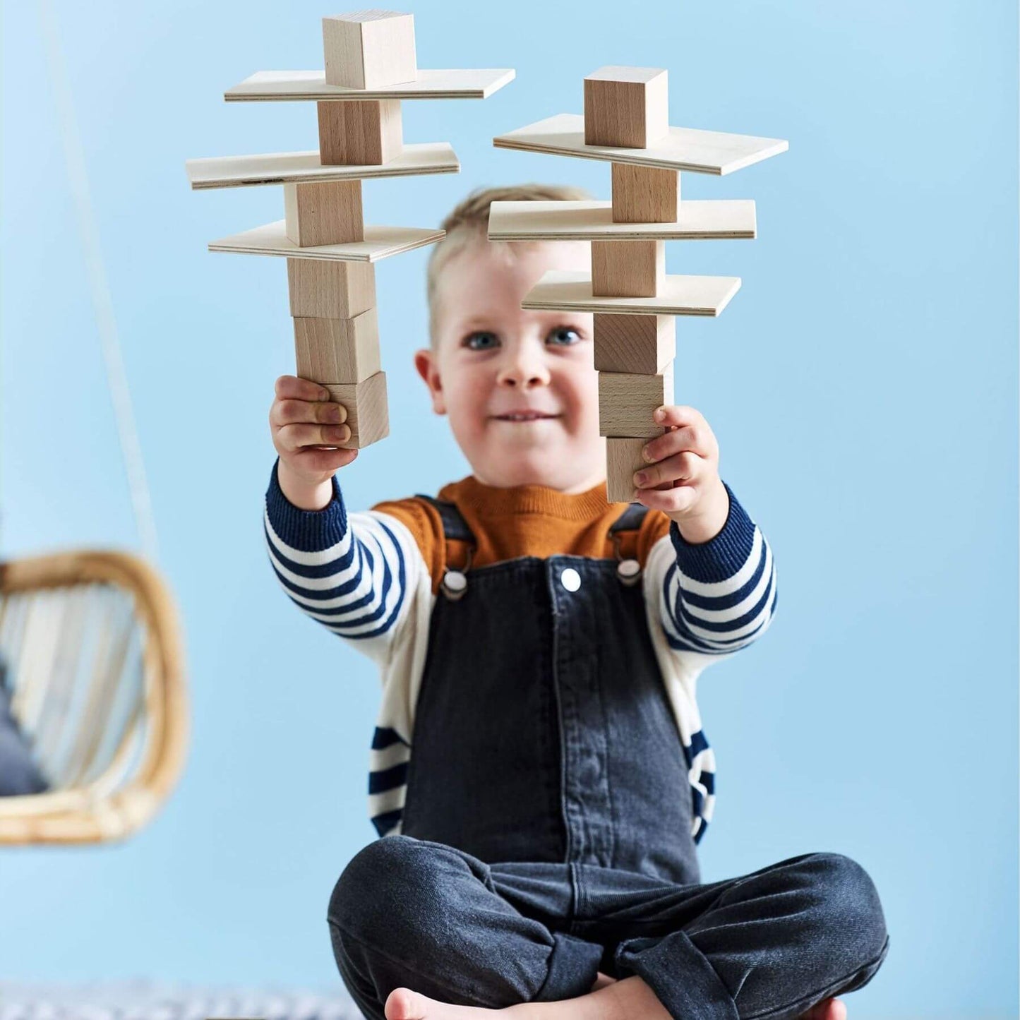 Child holding two wooden block structures against a light blue background