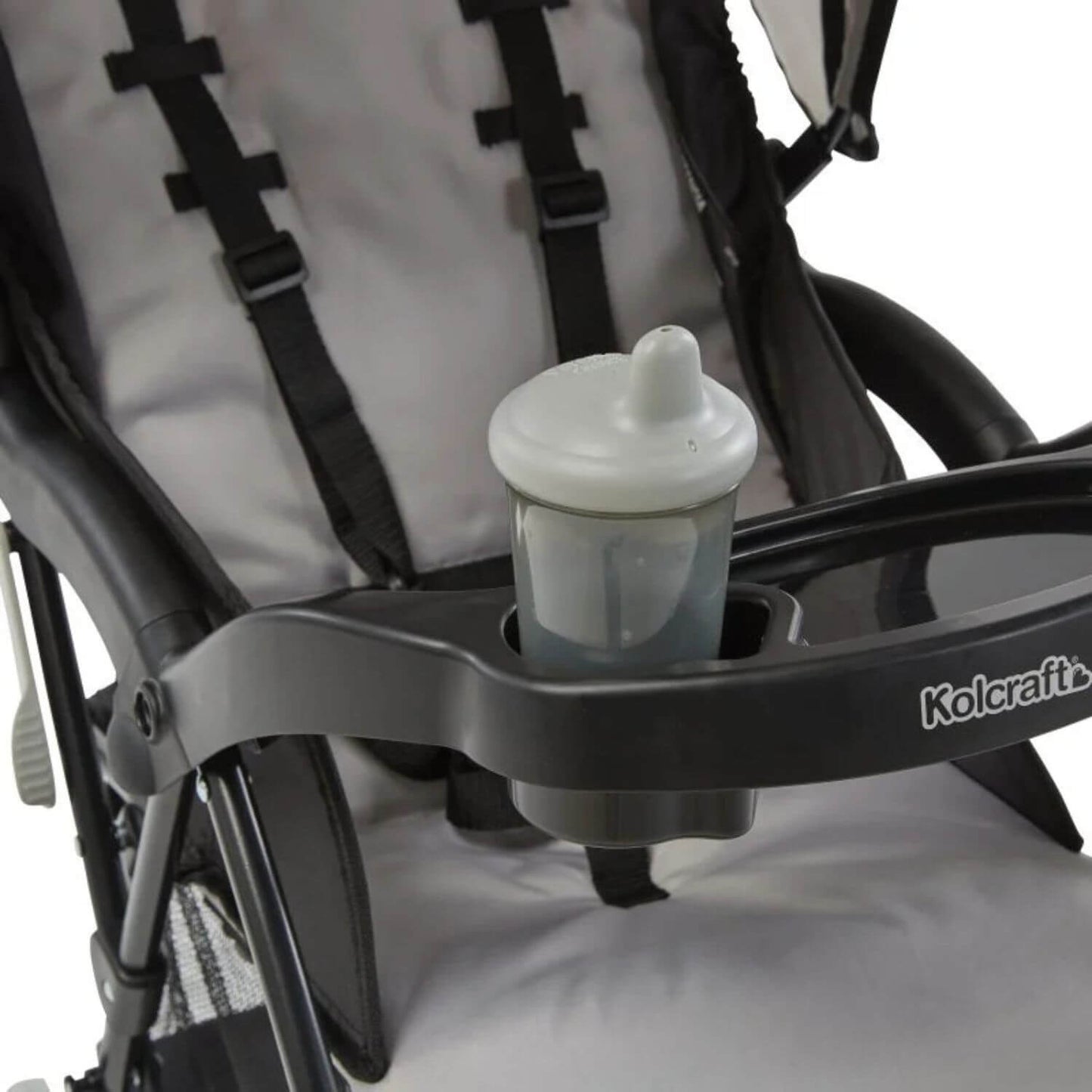 A close-up of a stroller with a black tray and cup holder, holding a white and translucent baby bottle. The stroller has a light gray and black fabric seat with black harness straps.