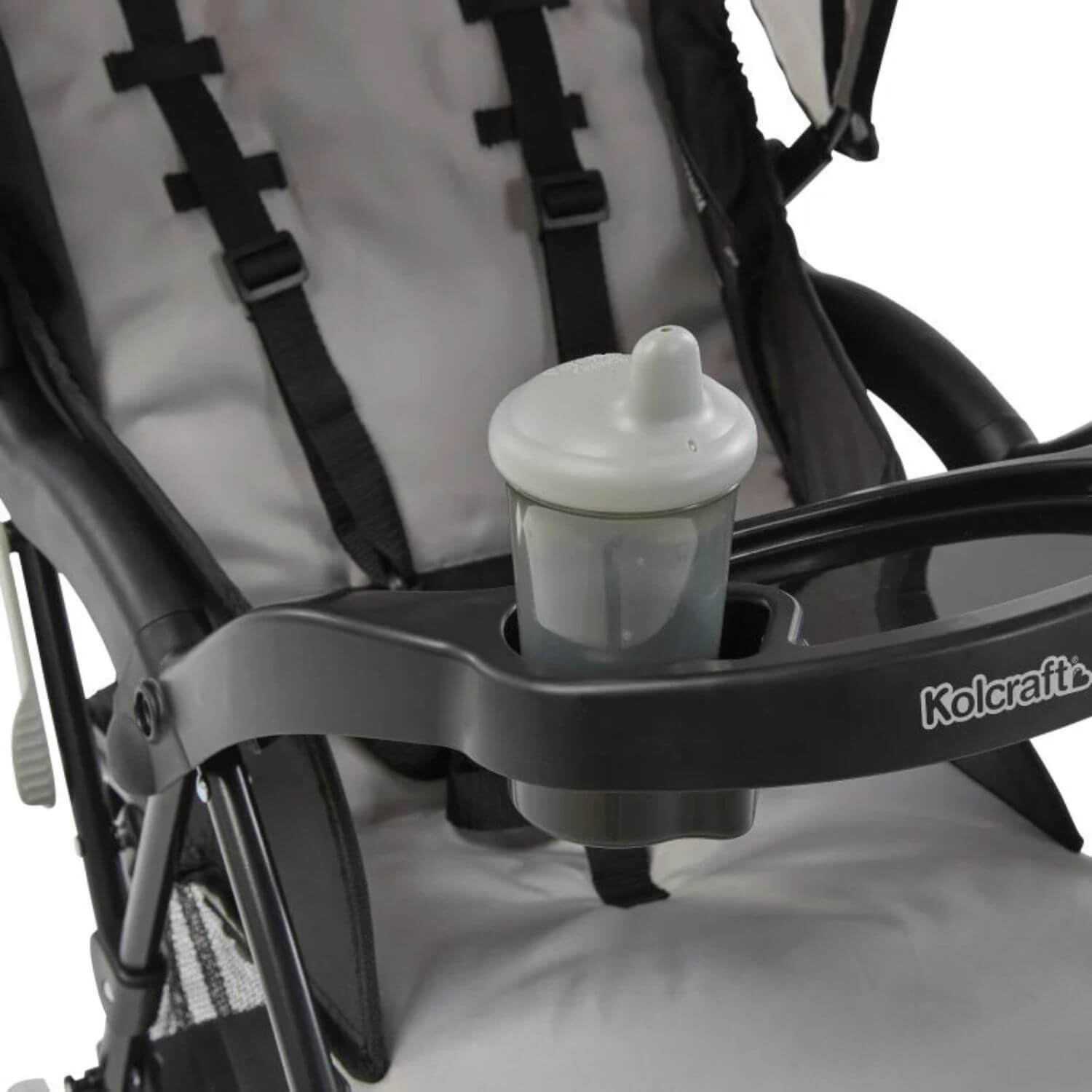 A close-up of a stroller with a black tray and cup holder, holding a white and translucent baby bottle. The stroller has a light gray and black fabric seat with black harness straps.