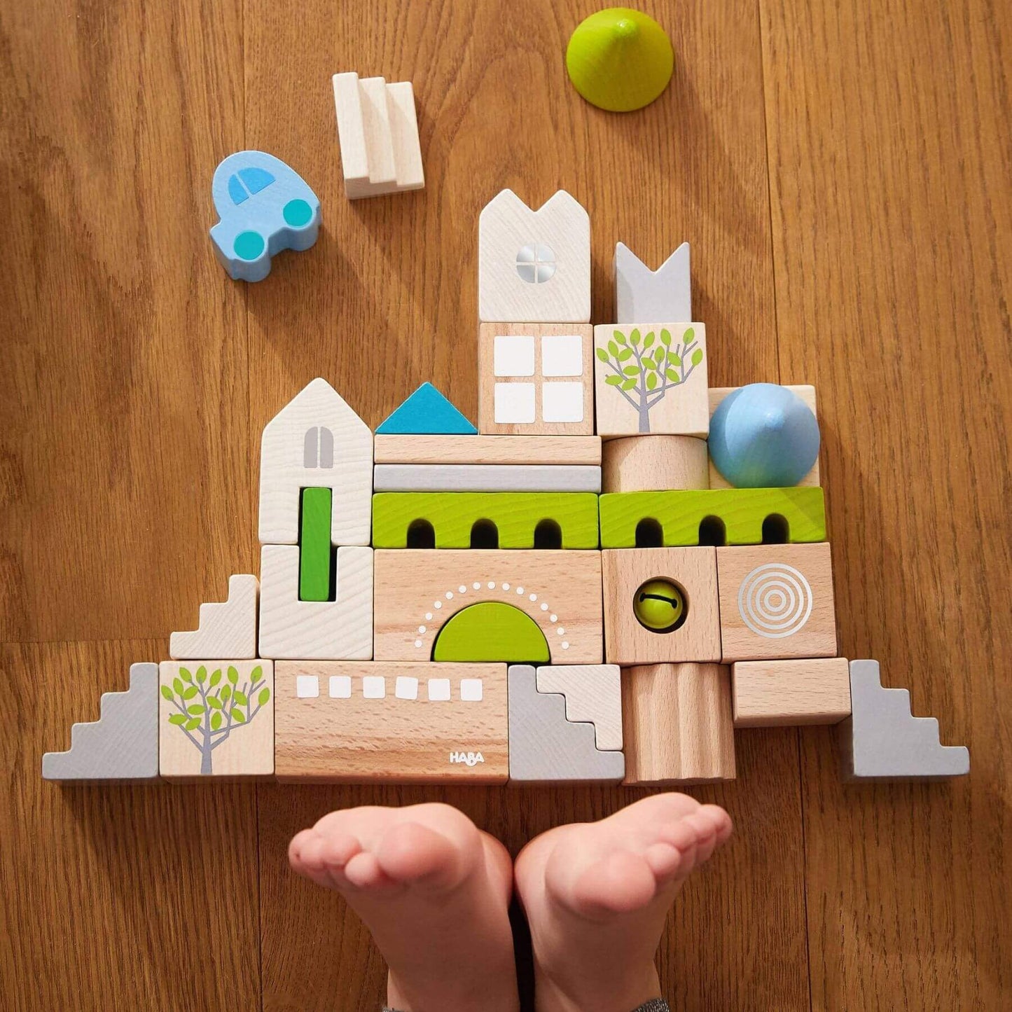 Wooden building blocks on a wooden surface with a child's feet visible.