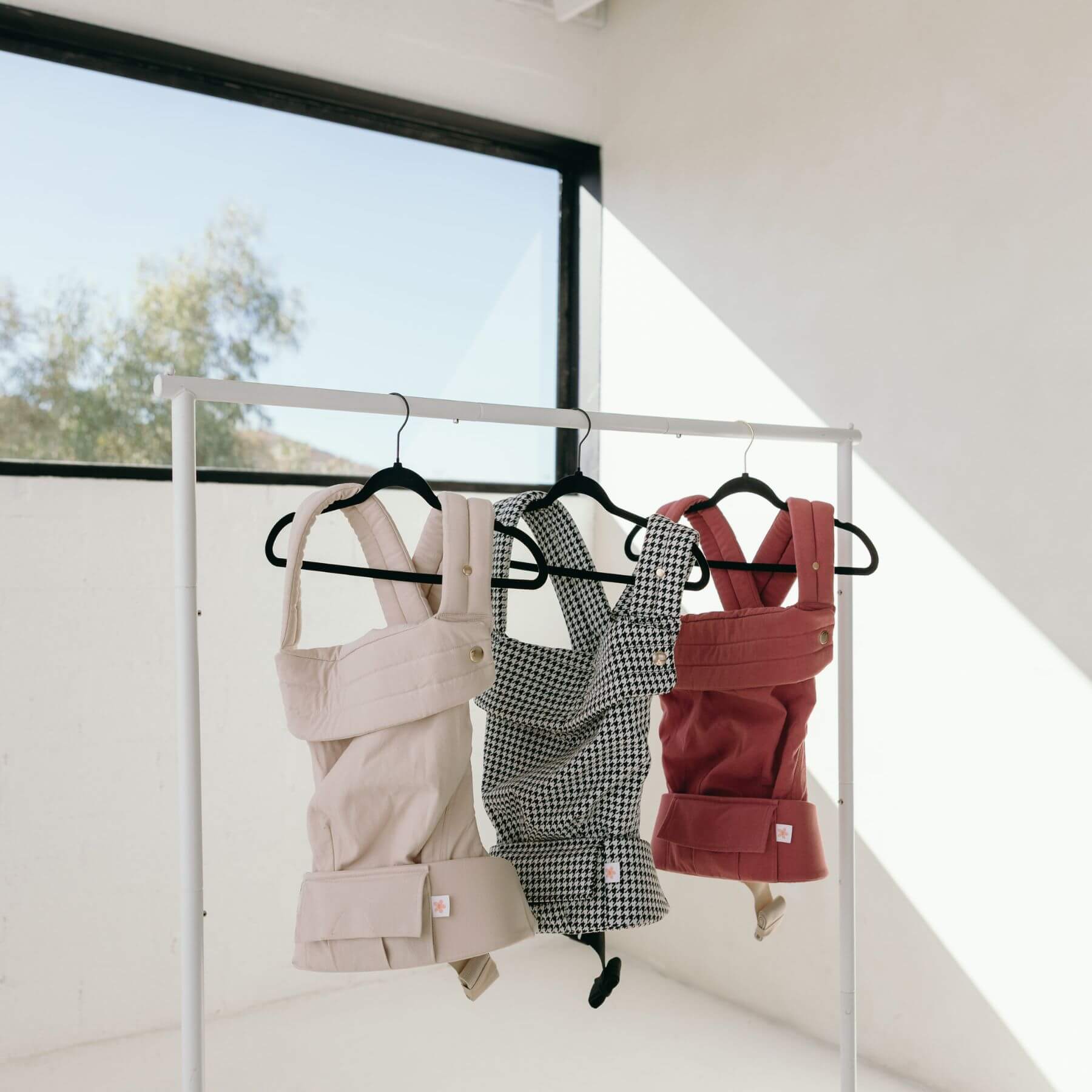 Three baby carriers against a white wall with a window in the background