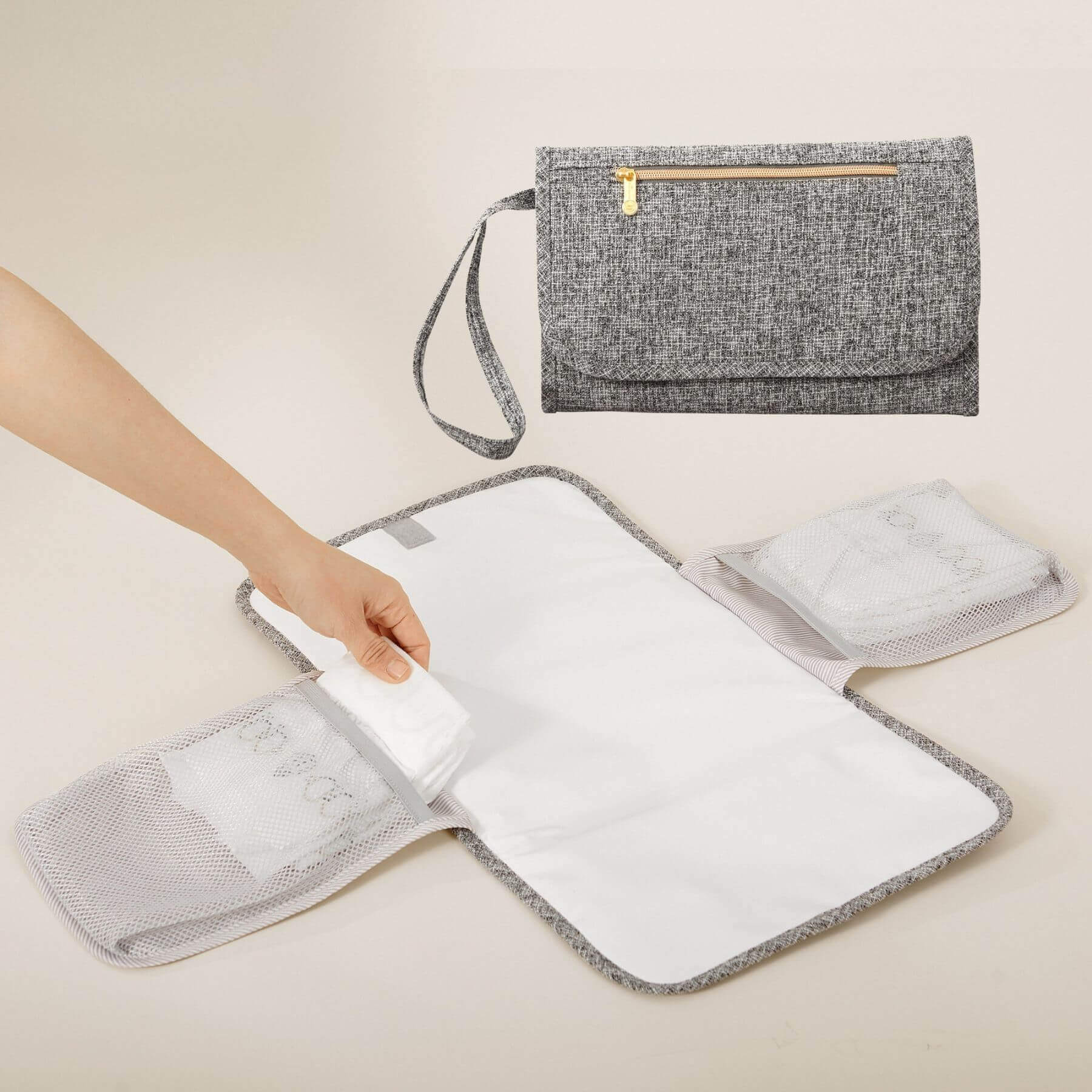 Gray diaper bag with a hand holding an open section, on a light beige background