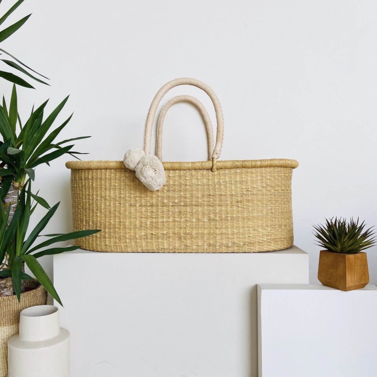 Plum+Sparrow Cream Handle No Hood Moses Basket with decorative items on a white surface with plants and a framed picture.