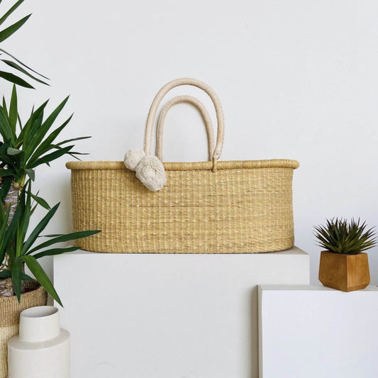 Plum+Sparrow Cream Handle No Hood Moses Basket with decorative items on a white surface with plants and a framed picture.