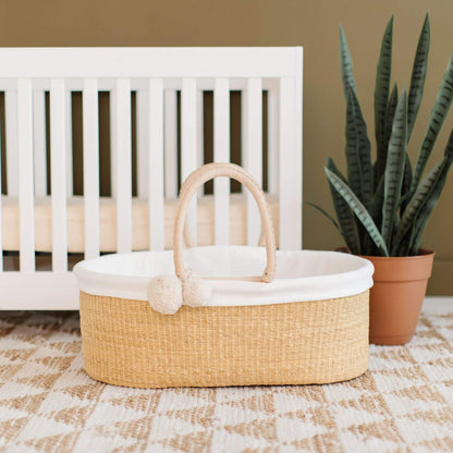 Plum+Sparrow Cream Handle No Hood Moses Basket on a checkered floor in front of a crib.