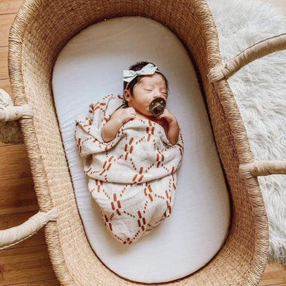 Newborn baby wrapped in a patterned blanket, sleeping peacefully in Plum+Sparrow Cream Handle No Hood Moses Basket