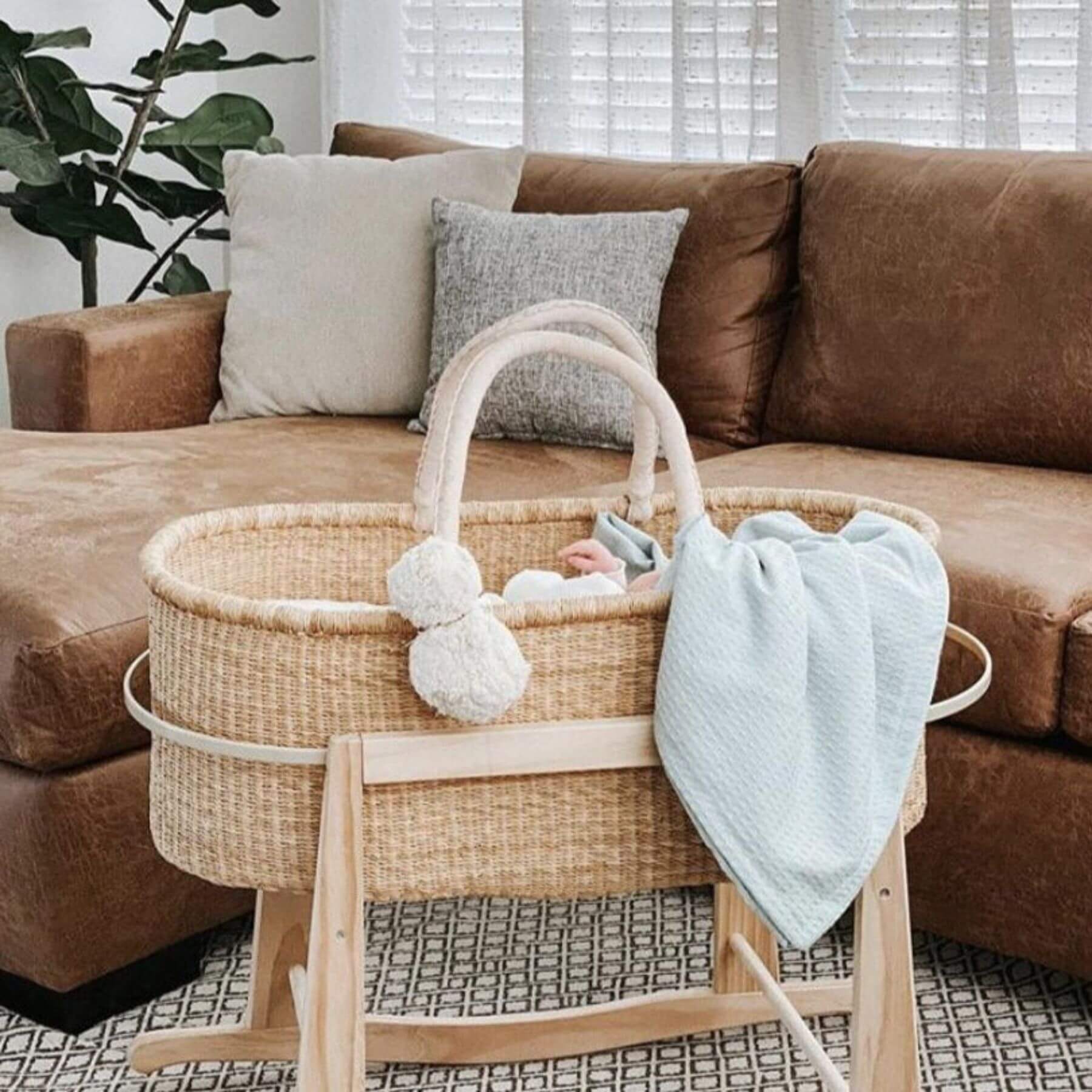 Plum+Sparrow Cream Handle No Hood Moses Basket with wooden stand on a brown sofa