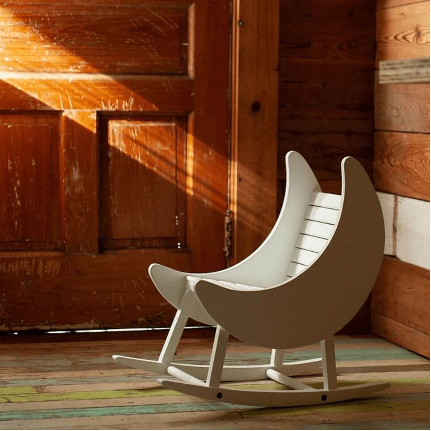 Wooden rocking chair shaped like a crescent moon in front of a wooden wall.