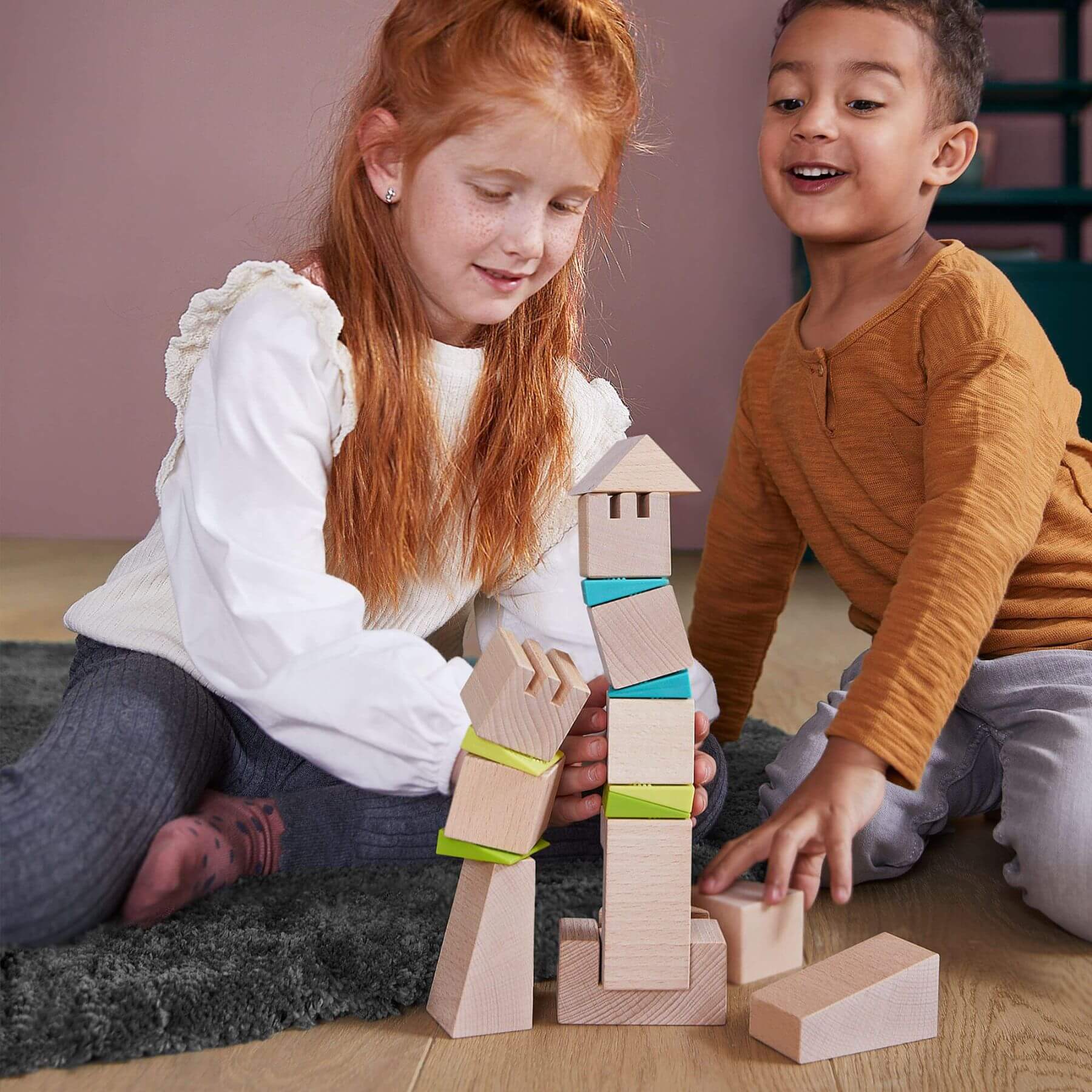 Two children playing with wooden blocks on a wooden floor.