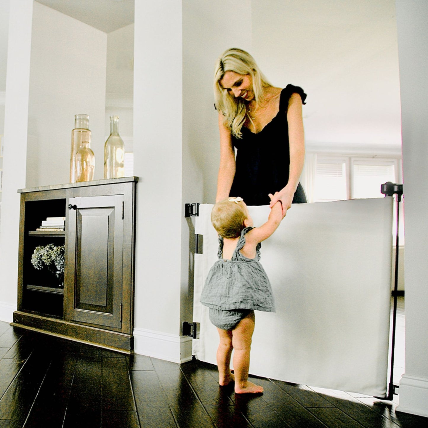 Woman helping a child climb over Crypton® Fabric Baby & Pet Safety Gate - Eggshell Black in a home setting