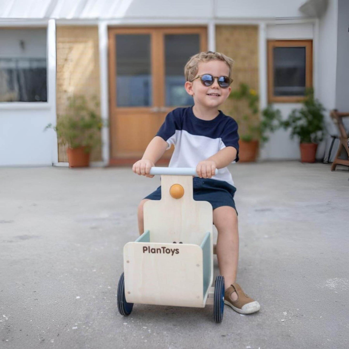 Child riding PlanToys Delivery Bike - Orchard with 'PlanToys' branding in an outdoor setting.
