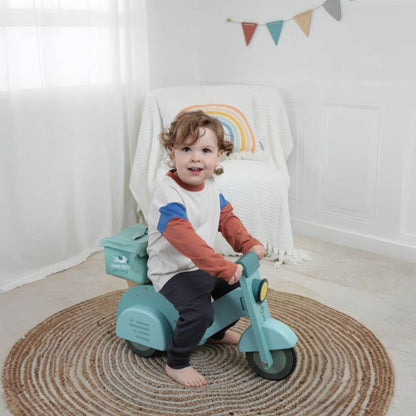 Child sitting on Tender Leaf Delivery Scooter in a room with a rainbow decoration.