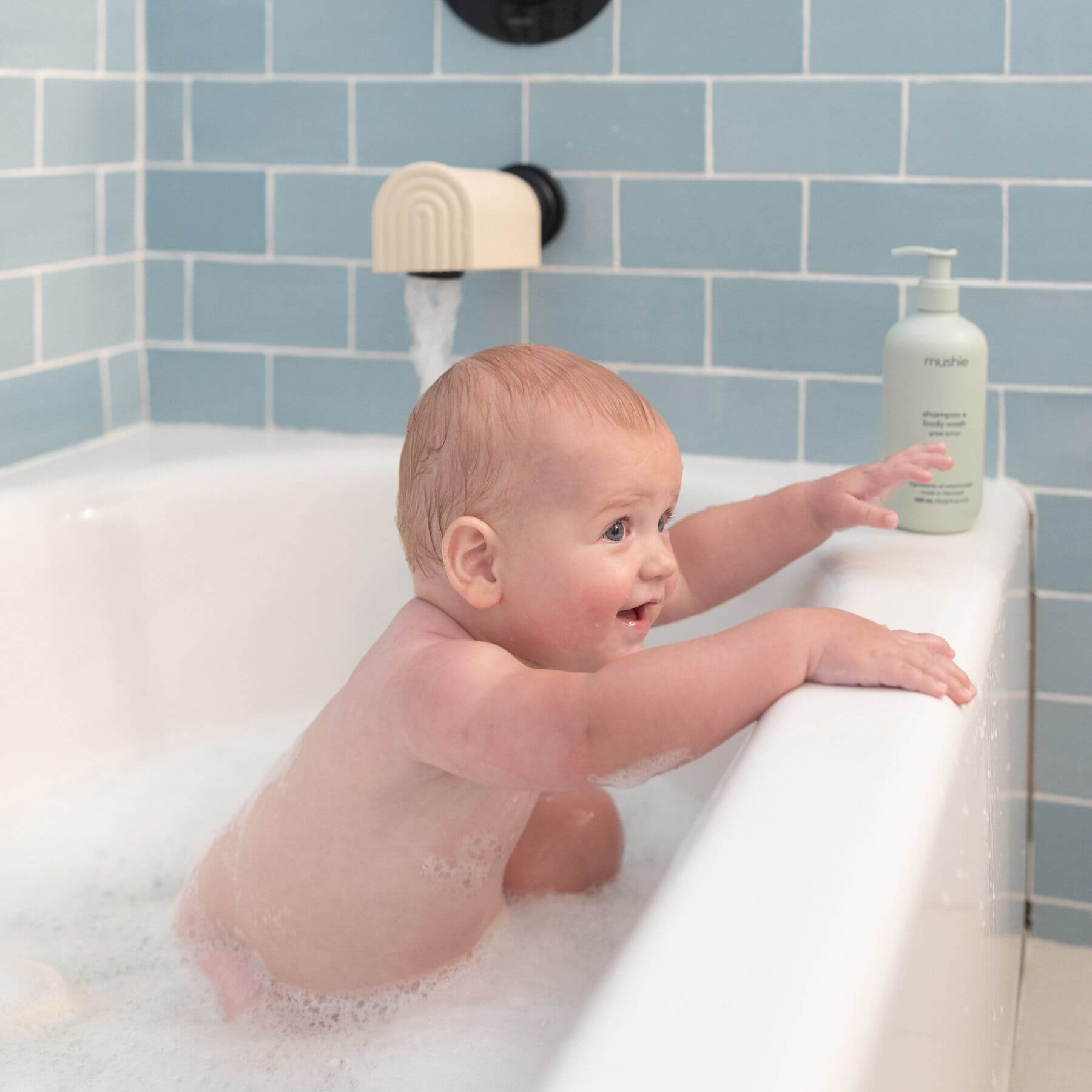 Baby in a bathtub with a bottle of shampoo on the edge