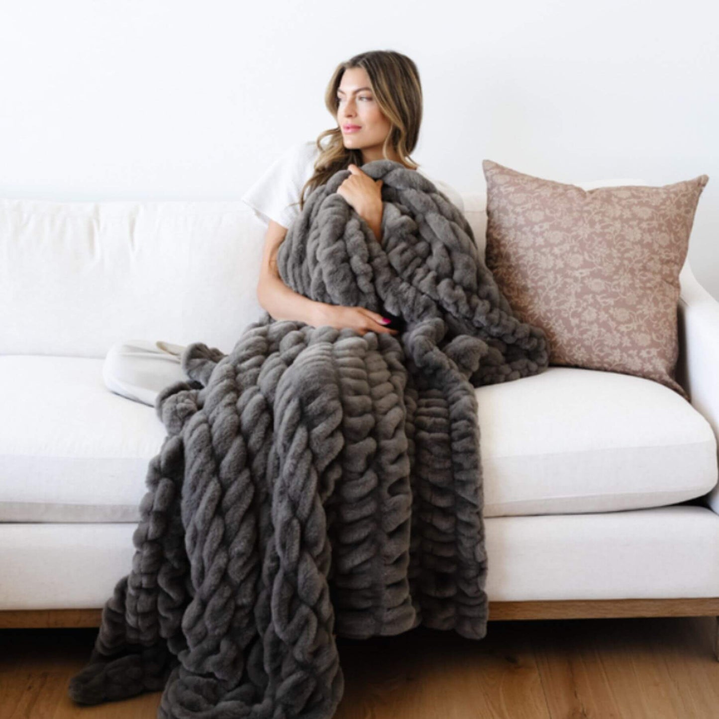 Woman sitting on a couch with Saranoni Double Ruched Faux Fur Throw Blankets Cobb draped over her