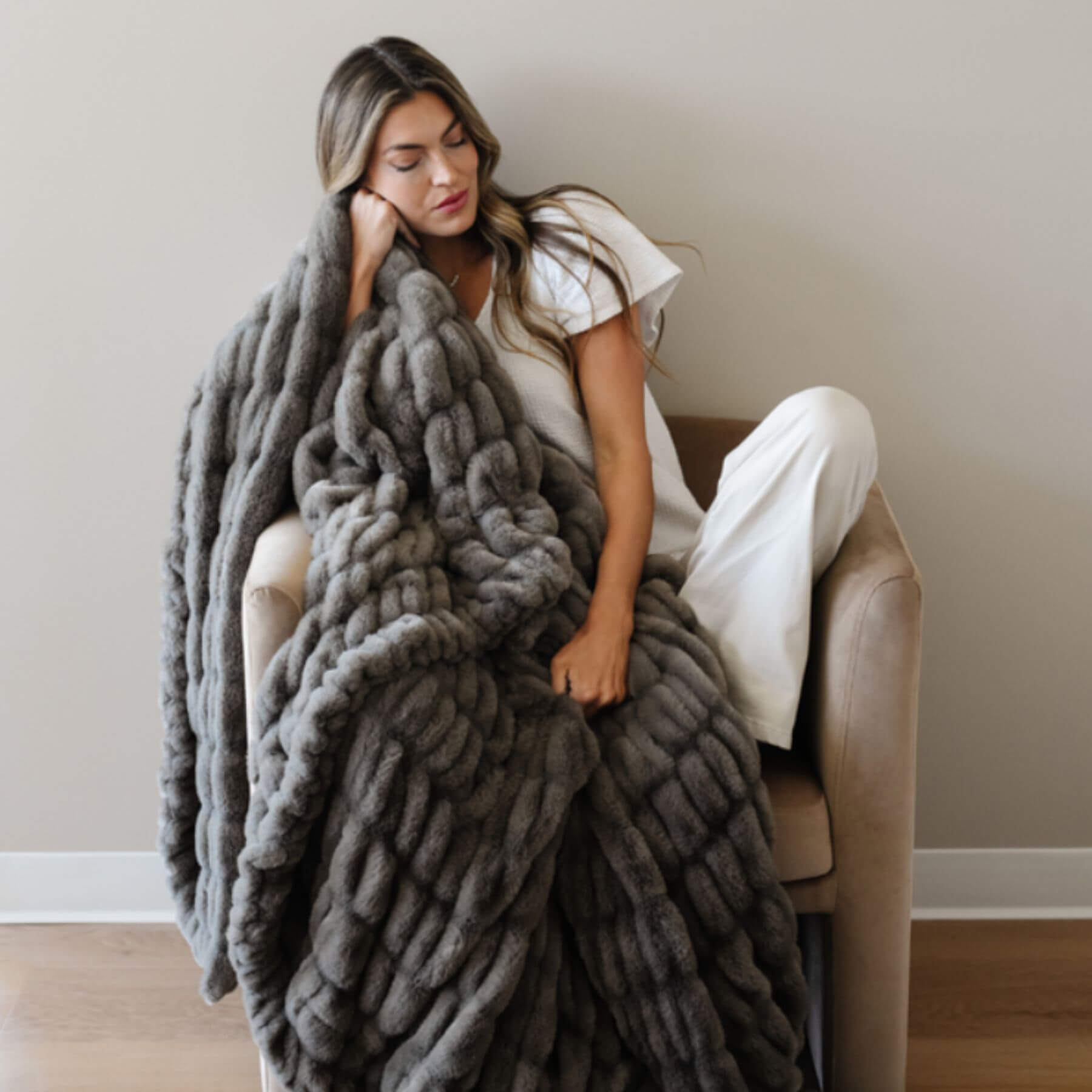 Woman sitting on a chair with Saranoni Double Ruched Faux Fur Throw Blankets Cobb draped over her
