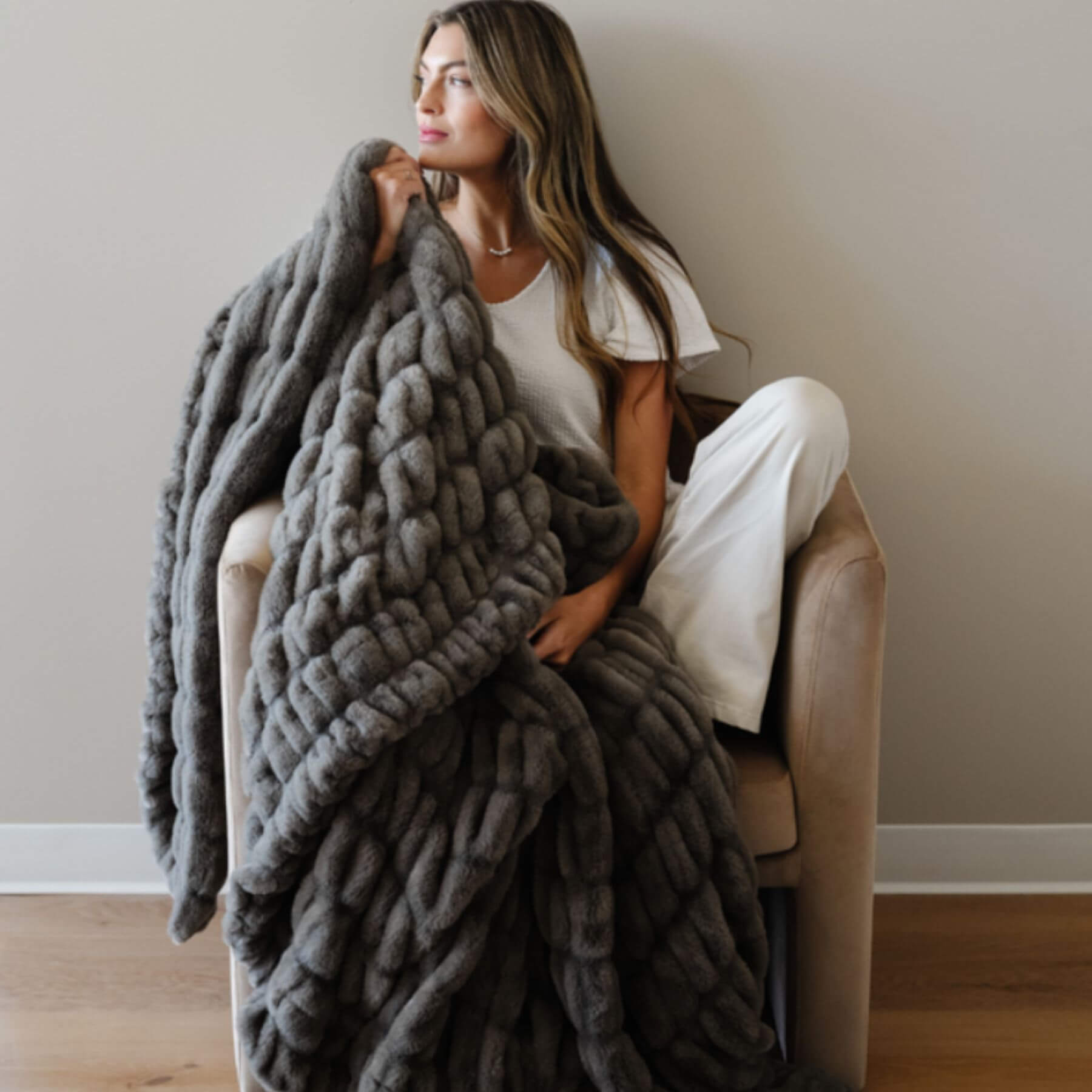 Woman sitting on a chair with Saranoni Double Ruched Faux Fur Throw Blankets Cobb draped over her