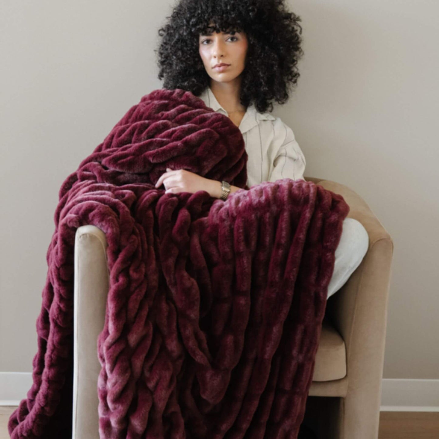 Woman sitting on a chair with Saranoni Double Ruched Faux Fur Throw Blankets Royale draped over her